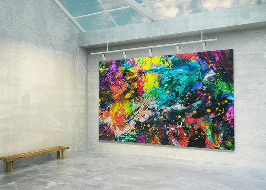 A large rectangular abstract canvas print with vivid splashes of blue, green, yellow, pink, purple, red, and orange displayed on a gallery wall in a modern concrete room with a wooden bench and skylight.