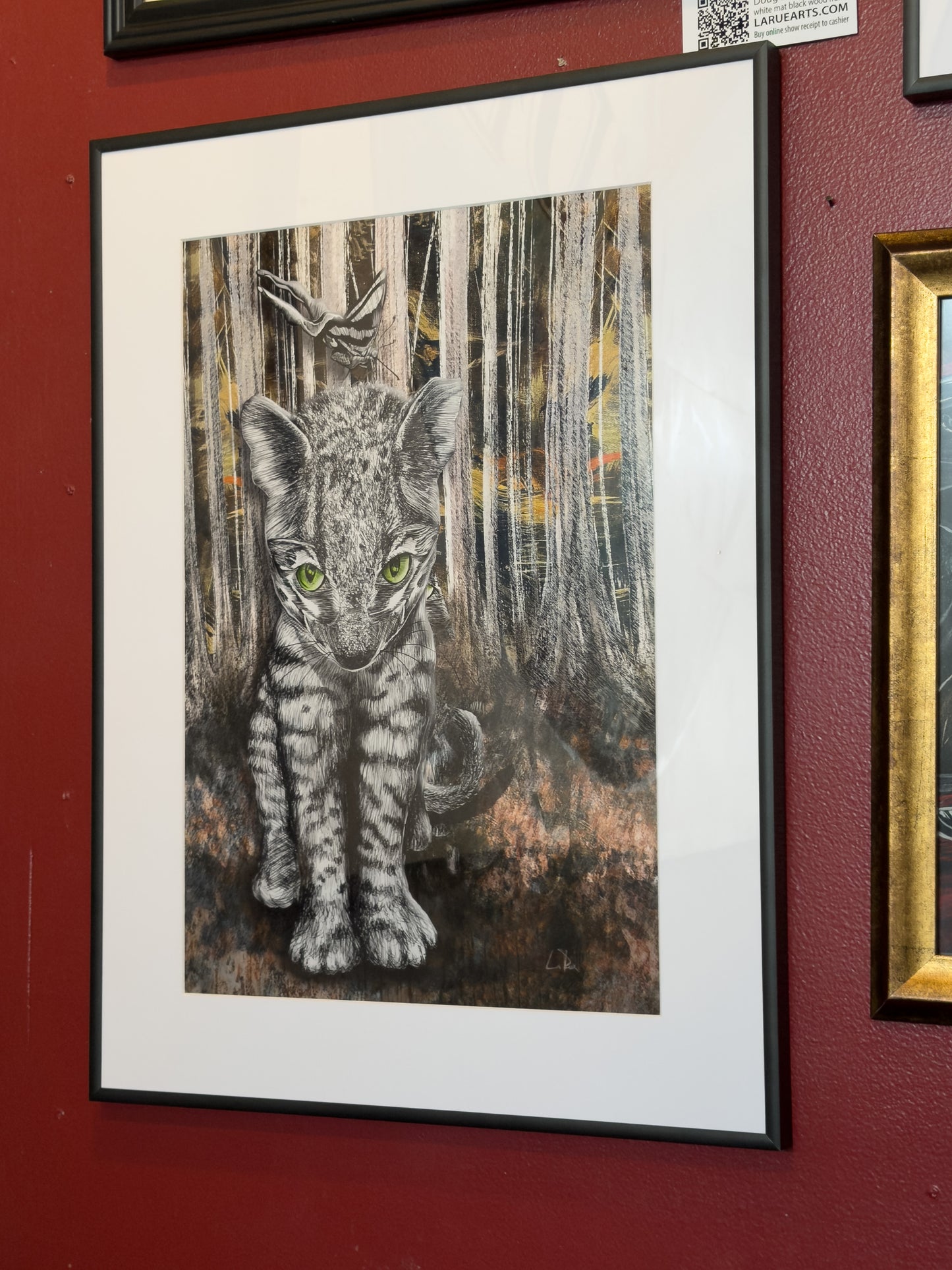 Framed artwork of a stylized cat in a forest setting on a red wall at NeWorld Gallery