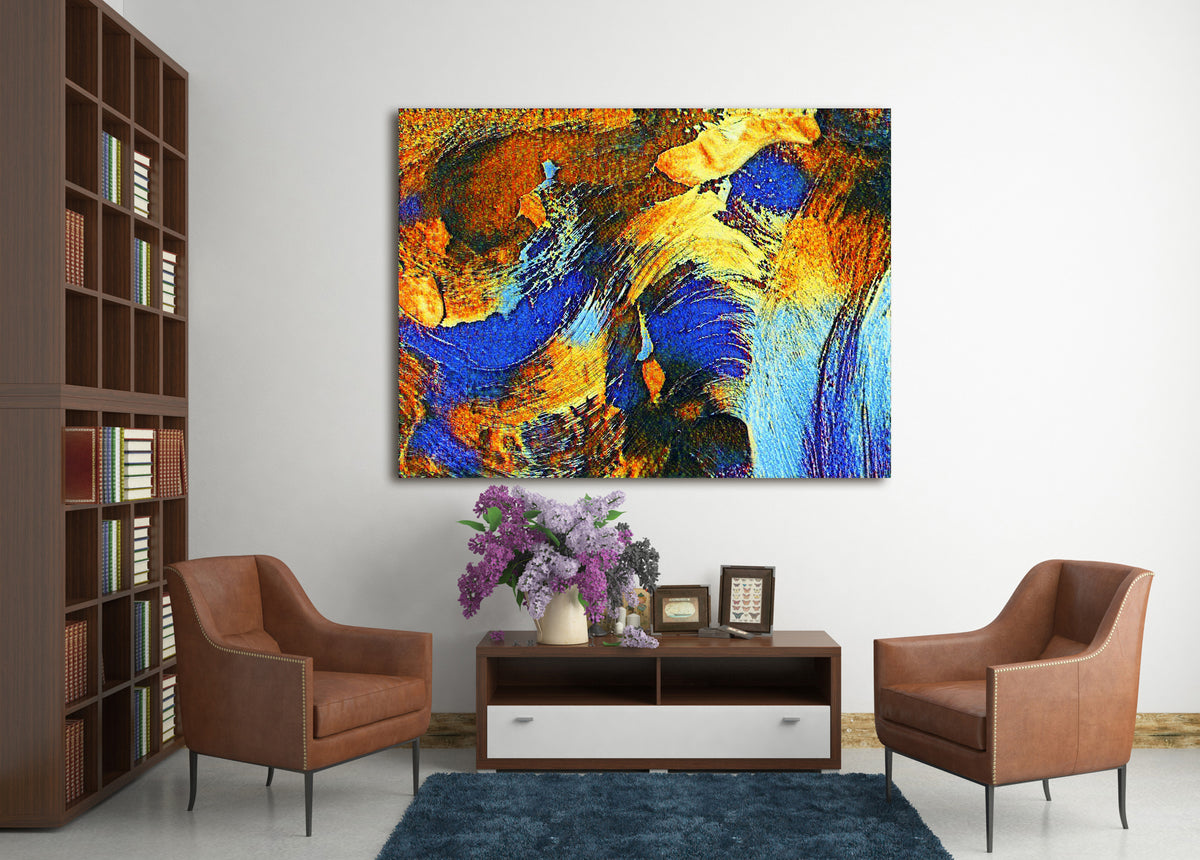 An abstract canvas wall art print featuring vibrant blue, gold, and orange brushstrokes, displayed in a modern living room setting above a wooden console table with two brown armchairs.
