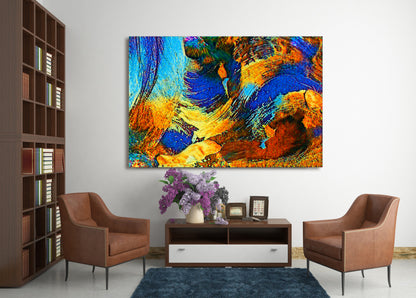 A large square abstract canvas print with vibrant blue, orange, yellow, and brown brushstrokes, displayed on a white wall in a modern living room setting with two brown armchairs and a dark wood console table. Rollingwood Cobalt by Doug LaRue
