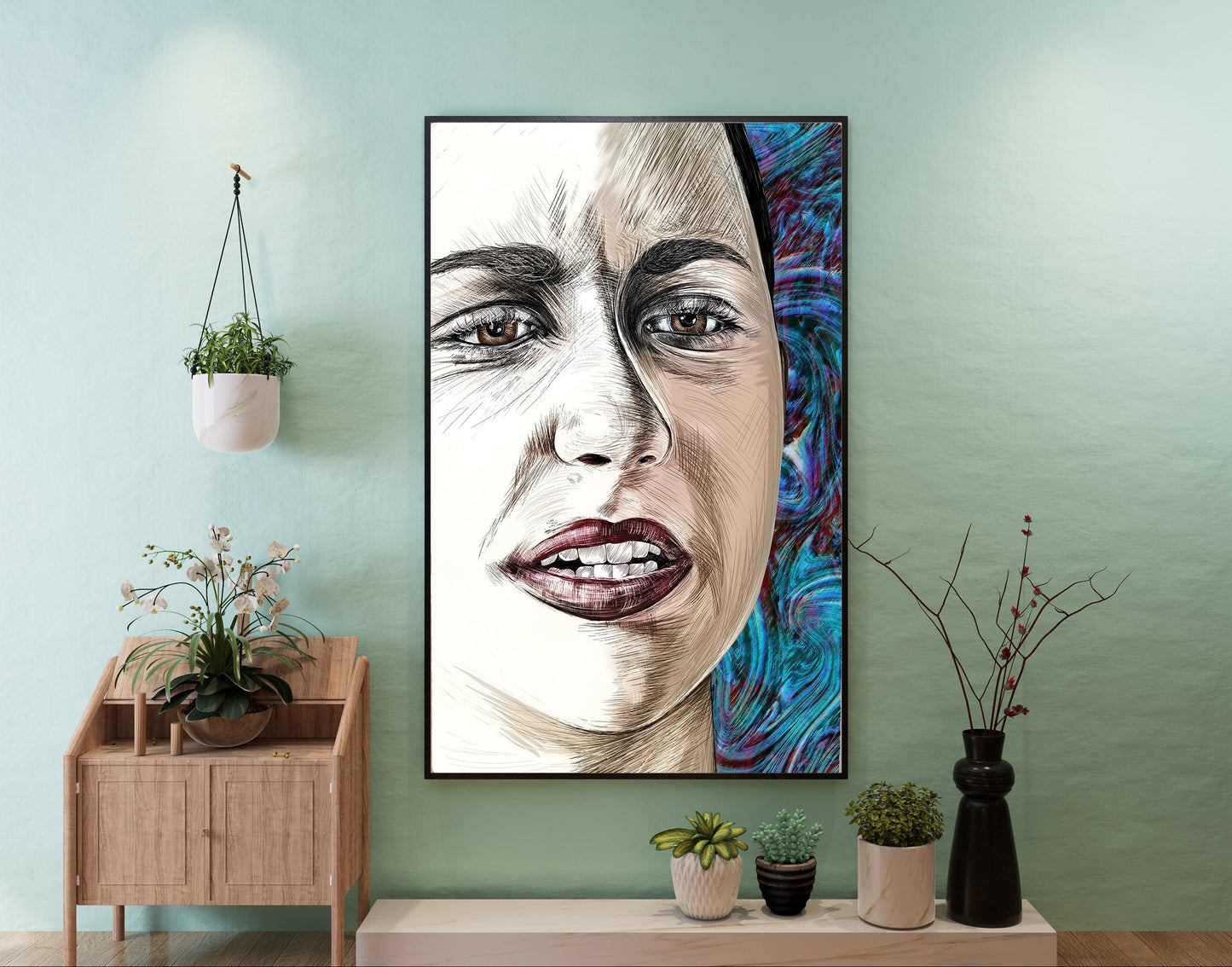 A framed vertical portrait painting of a woman's face hangs on a mint green wall above a light wood console table with small potted plants. The artwork features a detailed sketch-style face on the left and a vivid blue abstract background on the right. Emma Gonzales by Doug LaRue