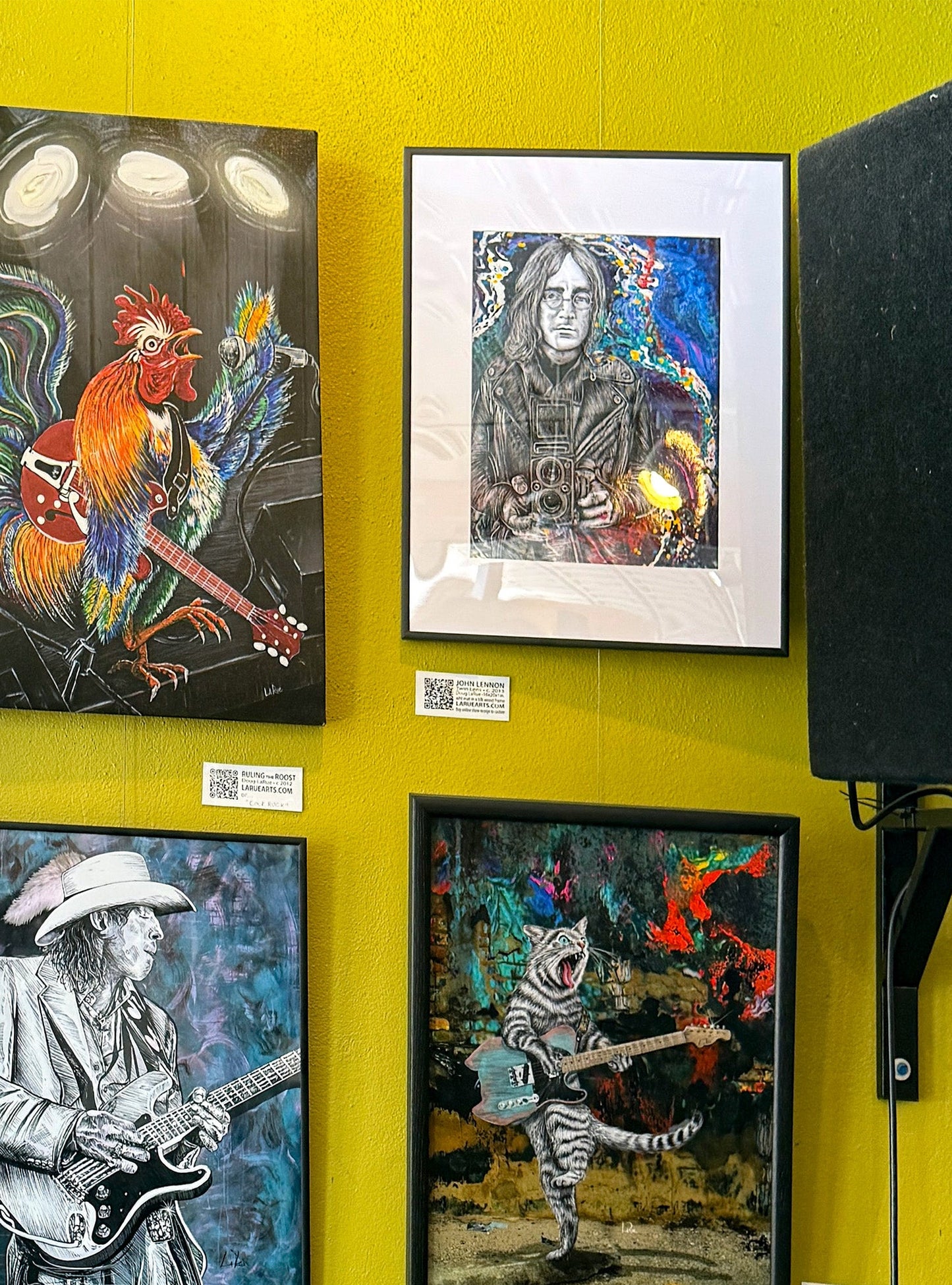 Four framed artworks on a yellow wall, featuring musicians and animals.