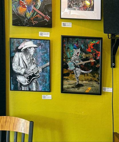 Four framed artworks on a yellow wall, featuring musicians and animals.