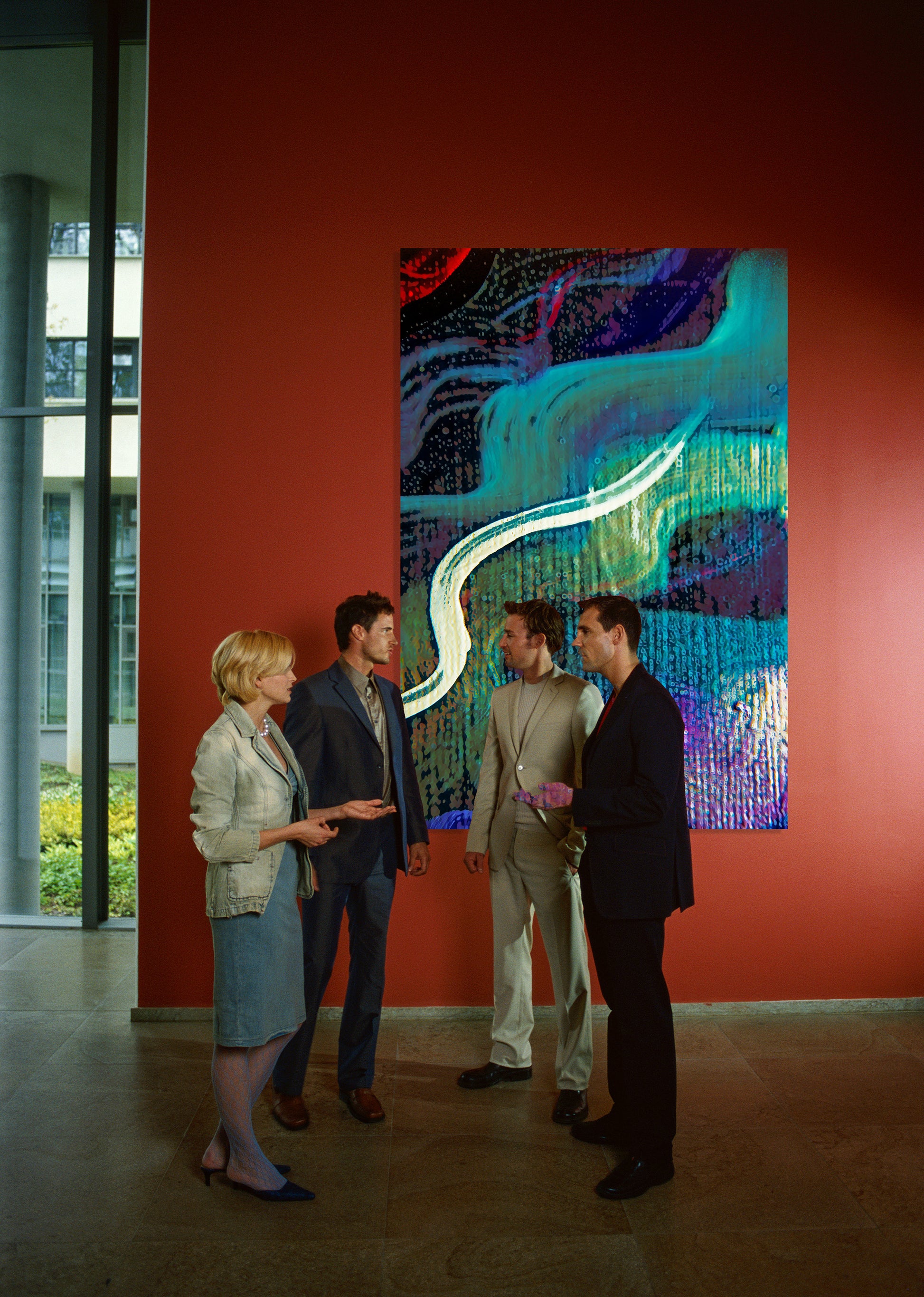 Four people standing and discussing a large abstract painting on a red wall in a gallery or museum setting. Lost Creek Feather art by Doug LaRue