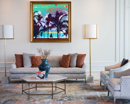 A framed tropical beach painting hangs on a white wall above a light gray sofa in a styled living room. The artwork shows dark palm tree silhouettes against turquoise water and sky with small red sun-like shapes.