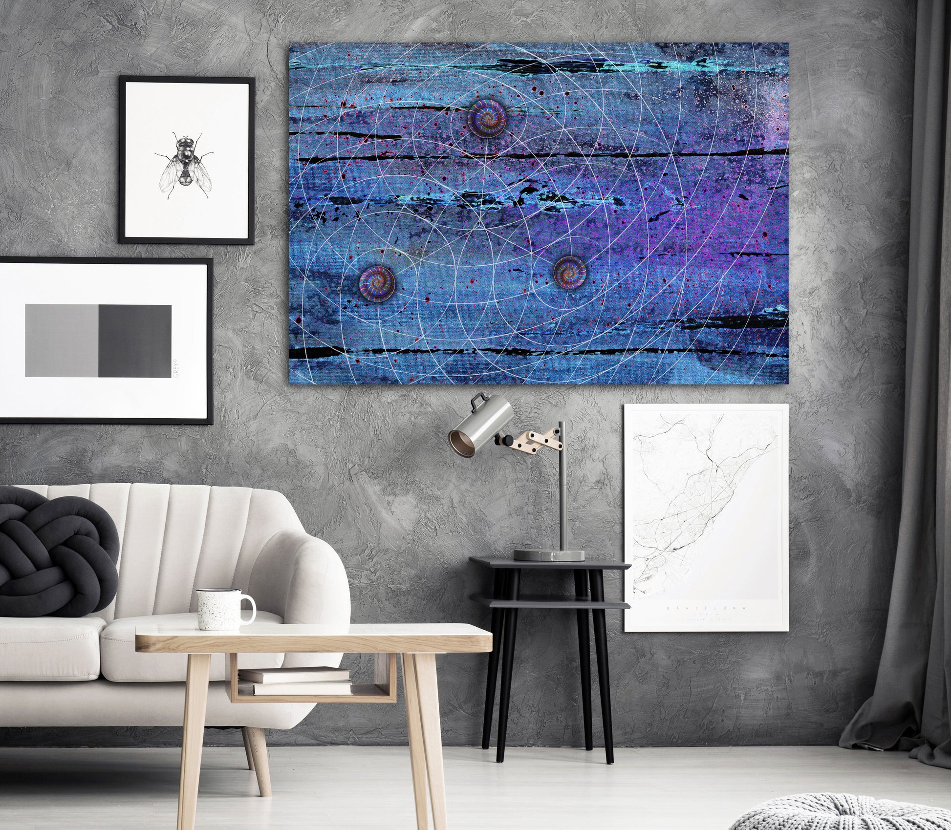 A large rectangular abstract wall art print featuring swirling blue, purple, and black tones with thin circular line patterns, displayed in a styled living room above a sofa and side table. Blue Trinity by Doug LaRue